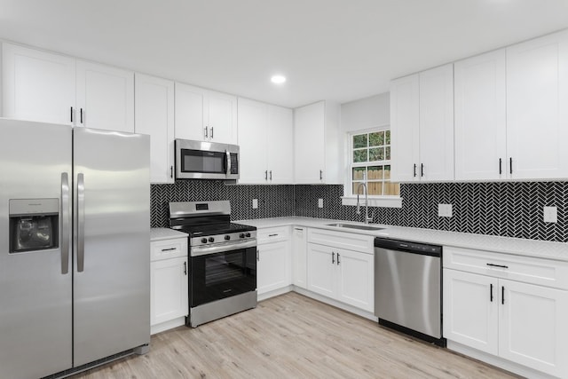 kitchen featuring appliances with stainless steel finishes, tasteful backsplash, white cabinets, light hardwood / wood-style flooring, and sink