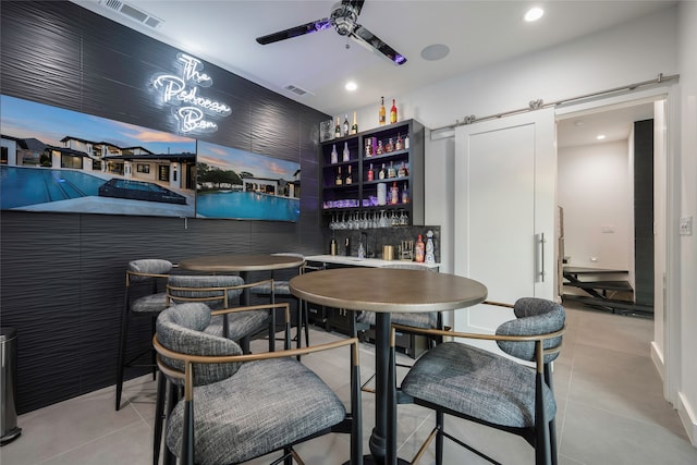 dining area featuring ceiling fan, a barn door, and indoor bar