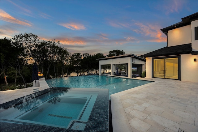 pool at dusk with a patio and an in ground hot tub