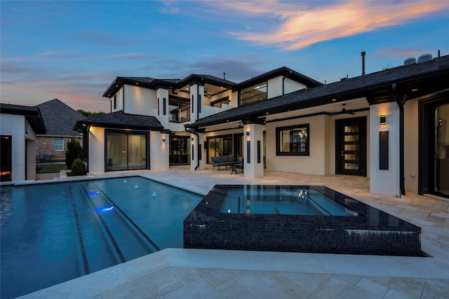 pool at dusk featuring a patio and an in ground hot tub