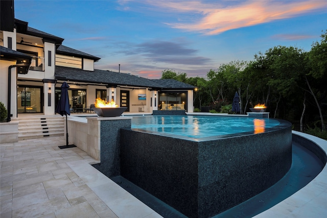 pool at dusk featuring a patio and pool water feature