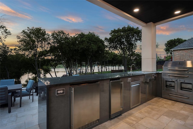 patio terrace at dusk with area for grilling and a water view