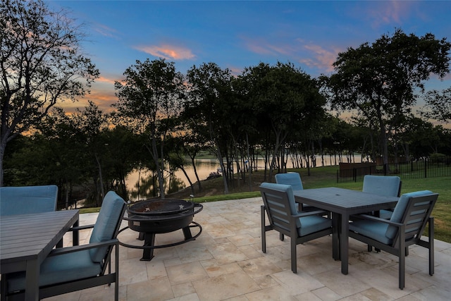 patio terrace at dusk featuring a water view, an outdoor fire pit, and a yard