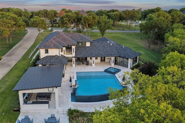 pool at dusk with an outdoor bar, an in ground hot tub, and a patio area