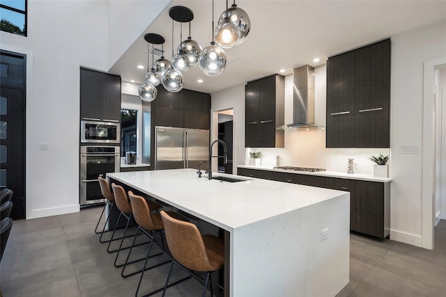 kitchen with an island with sink, hanging light fixtures, sink, wall chimney exhaust hood, and built in appliances