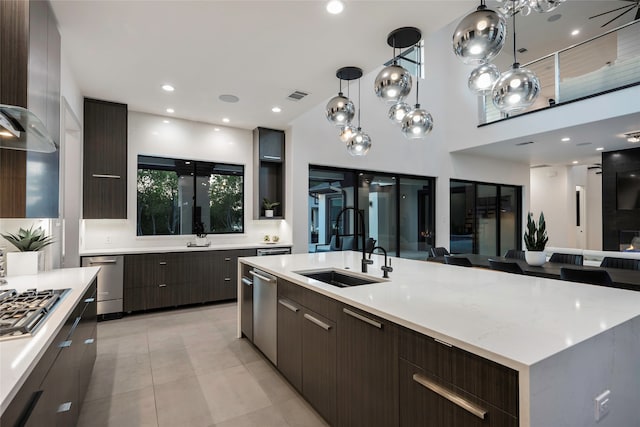 kitchen with light tile patterned flooring, a large island with sink, stainless steel gas stovetop, sink, and hanging light fixtures