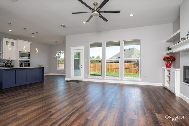 unfurnished living room featuring dark hardwood / wood-style floors, ceiling fan, and sink