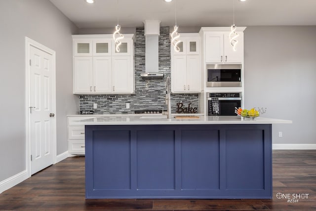 kitchen with a center island with sink, oven, white cabinetry, and hanging light fixtures