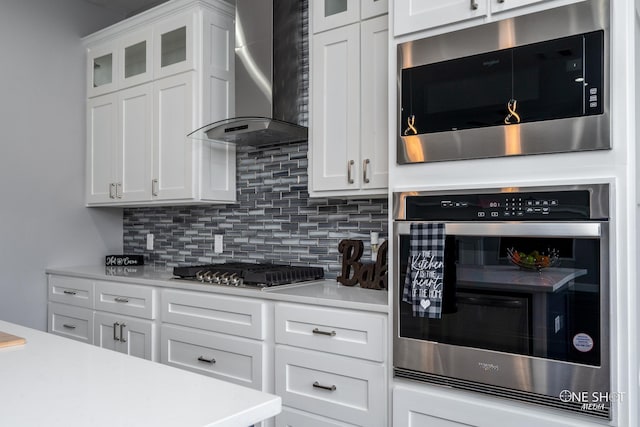 kitchen with decorative backsplash, stainless steel appliances, white cabinetry, and wall chimney exhaust hood