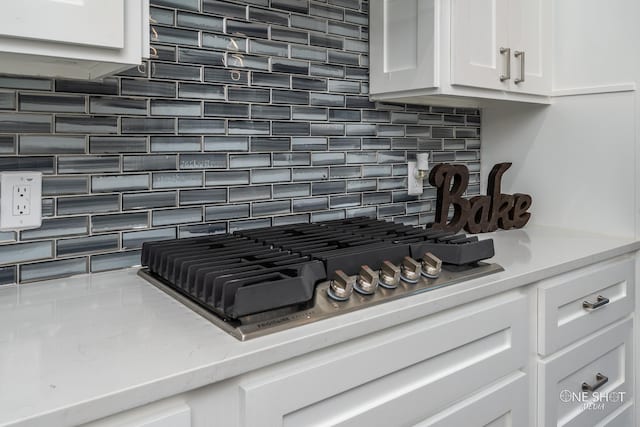 interior details with tasteful backsplash, white cabinetry, stainless steel gas cooktop, and light stone counters