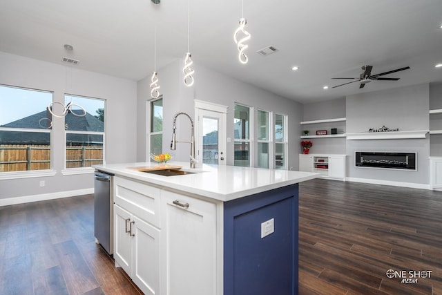 kitchen featuring sink, decorative light fixtures, built in features, white cabinetry, and an island with sink