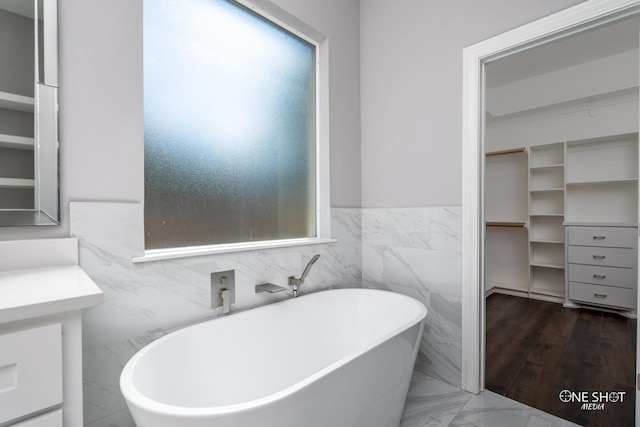 bathroom featuring a tub to relax in, vanity, and tile walls