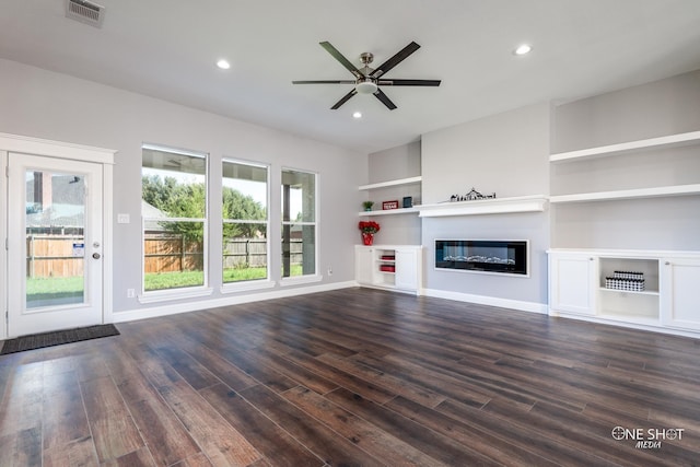 unfurnished living room with built in shelves, dark hardwood / wood-style floors, plenty of natural light, and ceiling fan