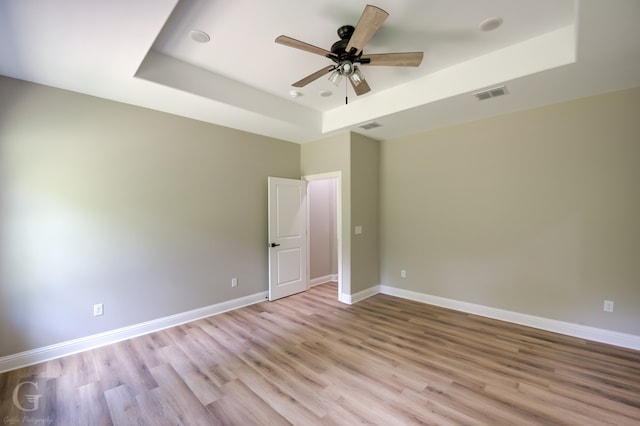 spare room featuring light hardwood / wood-style floors, ceiling fan, and a tray ceiling