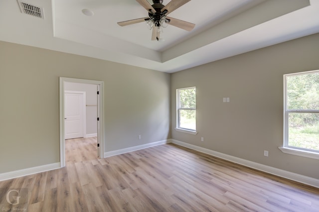 empty room featuring light wood-type flooring, ceiling fan, and a tray ceiling