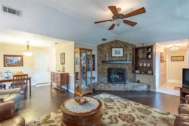 living room with vaulted ceiling, a brick fireplace, ceiling fan with notable chandelier, a textured ceiling, and hardwood / wood-style flooring