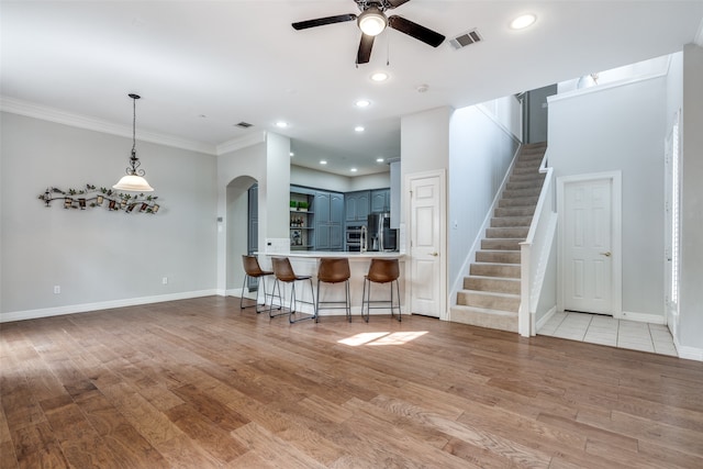 unfurnished living room with ceiling fan, ornamental molding, and light wood-type flooring