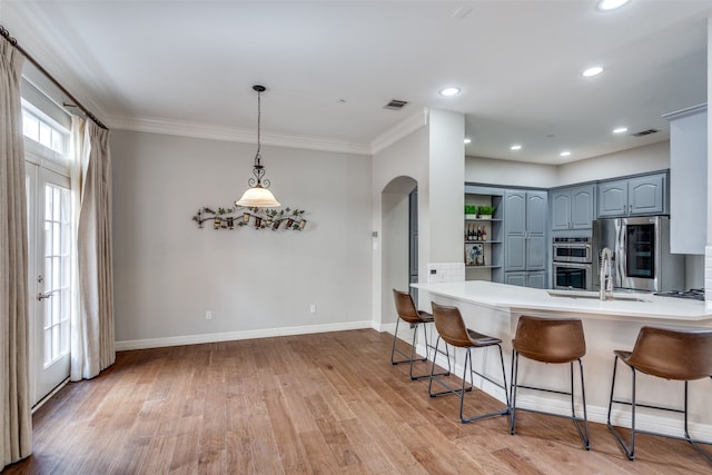 kitchen with kitchen peninsula, light wood-type flooring, ornamental molding, stainless steel appliances, and hanging light fixtures