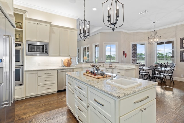 kitchen with an island with sink, stainless steel appliances, decorative light fixtures, sink, and a chandelier