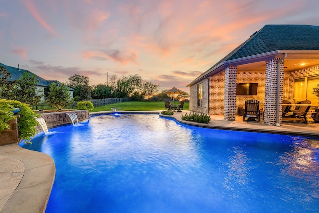 pool at dusk featuring a patio area, pool water feature, and a yard