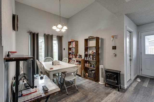 dining room featuring dark wood-type flooring, a wood stove, a textured ceiling, lofted ceiling, and a notable chandelier