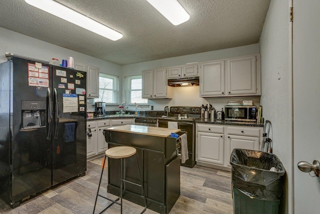 613 Purple Sage Trl, Mesquite, TX 75149 - kitchen with black appliances, under cabinet range hood, light wood finished floors, dark countertops, and a textured ceiling