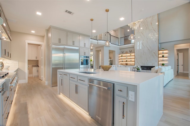 kitchen with sink, an island with sink, hanging light fixtures, a fireplace, and stainless steel appliances