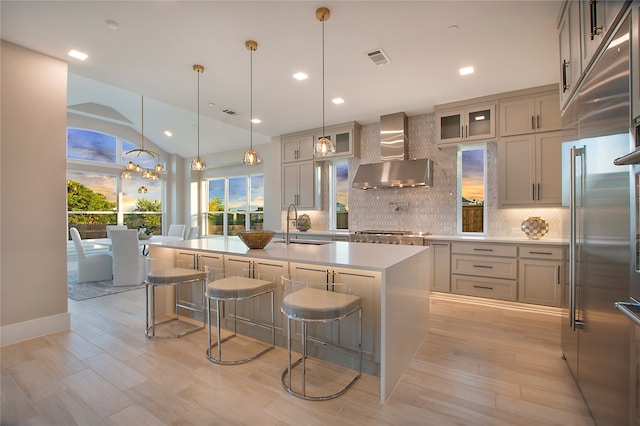 kitchen featuring pendant lighting, a center island with sink, wall chimney range hood, and a breakfast bar area