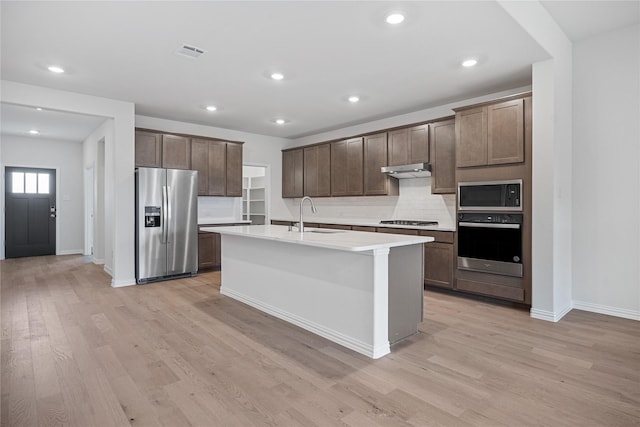 kitchen featuring sink, light hardwood / wood-style flooring, an island with sink, stainless steel appliances, and decorative backsplash