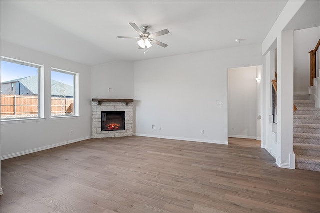 unfurnished living room with ceiling fan, lofted ceiling, a stone fireplace, and light wood-type flooring