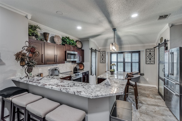 kitchen featuring kitchen peninsula, stainless steel appliances, a barn door, decorative light fixtures, and a breakfast bar area