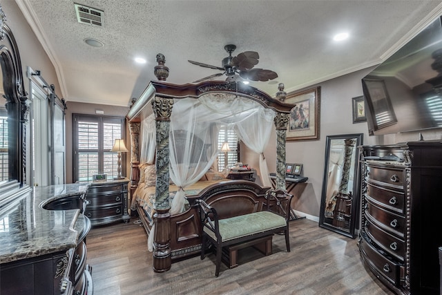 bedroom with hardwood / wood-style flooring, a barn door, ornamental molding, and a textured ceiling