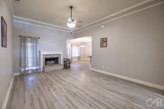 unfurnished living room featuring ceiling fan with notable chandelier, a brick fireplace, light hardwood / wood-style flooring, and crown molding