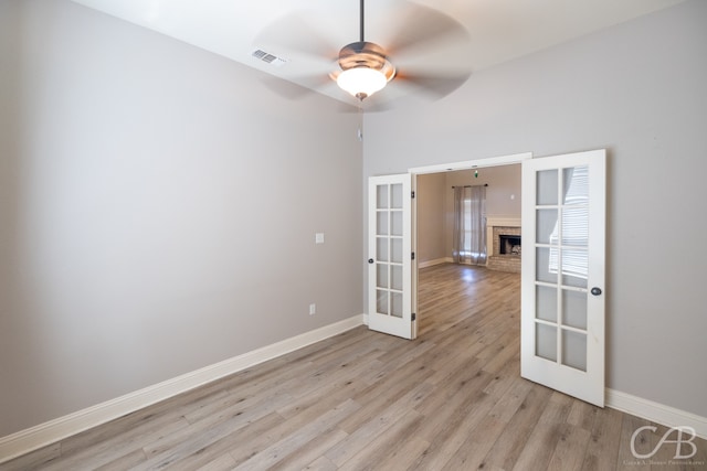 unfurnished room featuring a fireplace, ceiling fan, french doors, and light hardwood / wood-style flooring