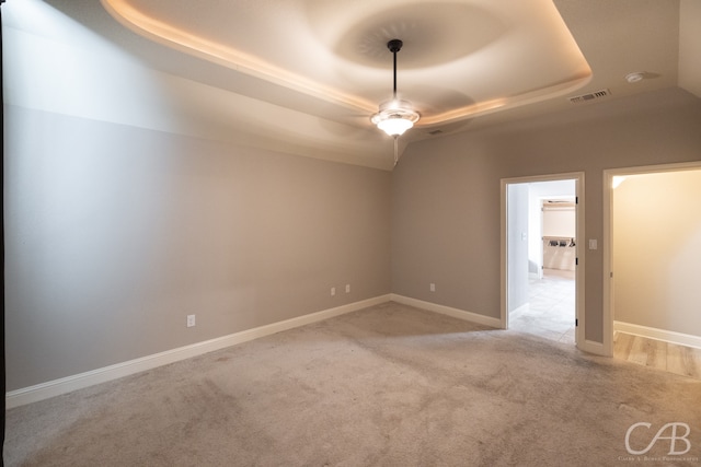 spare room with a tray ceiling, ceiling fan, and light colored carpet