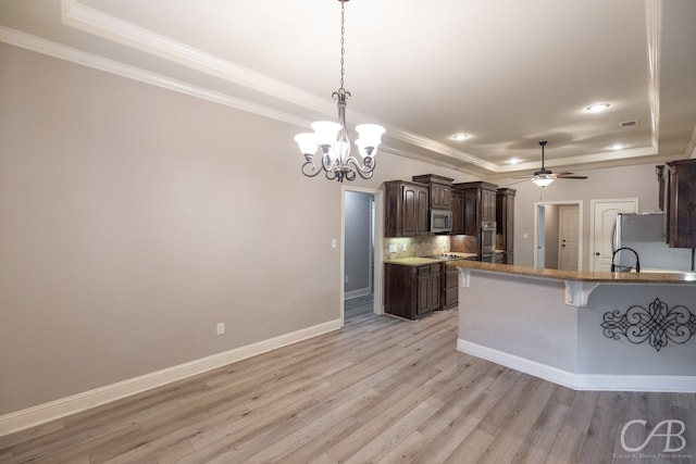 kitchen with stainless steel appliances, a tray ceiling, a breakfast bar area, ceiling fan with notable chandelier, and light hardwood / wood-style floors