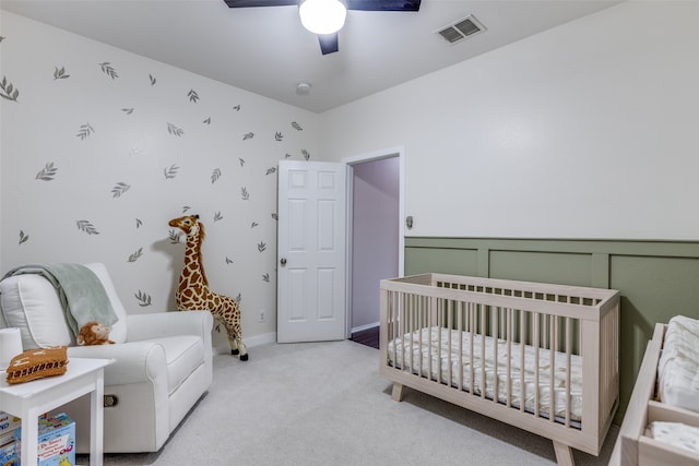 carpeted bedroom with ceiling fan and a nursery area