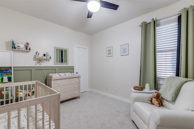 bedroom with a crib, light carpet, ceiling fan, and a closet