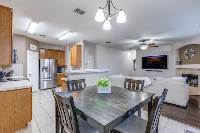 dining room with ceiling fan with notable chandelier, a tiled fireplace, and light hardwood / wood-style floors