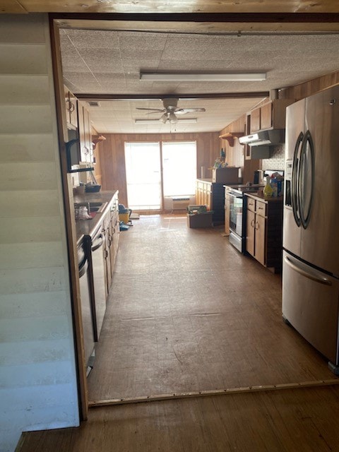 kitchen with wooden walls, ceiling fan, range with electric cooktop, and stainless steel fridge