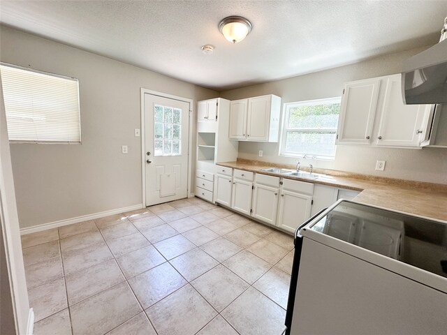 kitchen featuring white cabinets, light tile patterned floors, a textured ceiling, stove, and sink