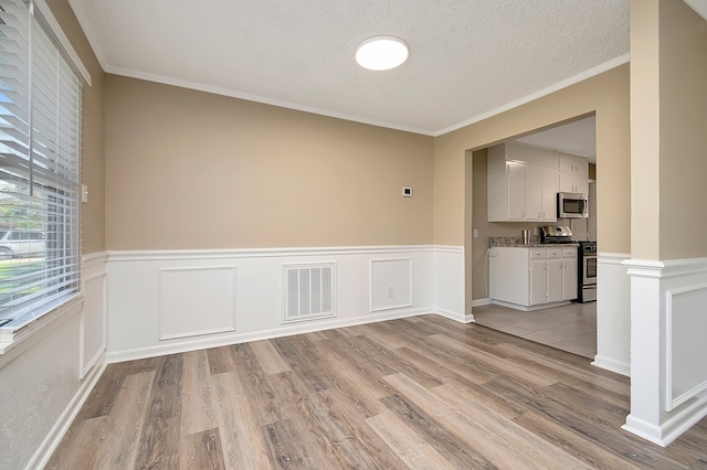 empty room featuring a textured ceiling, crown molding, and light hardwood / wood-style floors