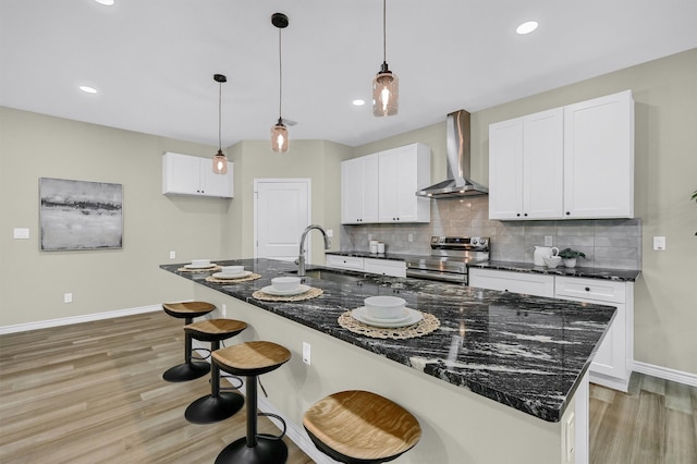 kitchen featuring wall chimney range hood, stainless steel electric range, and white cabinets