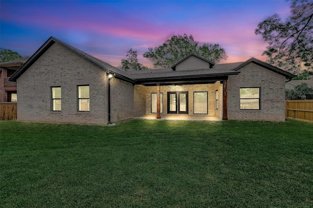 back house at dusk featuring a lawn and a patio area