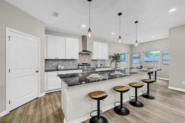 kitchen with an island with sink, stainless steel electric range, wall chimney exhaust hood, and white cabinets