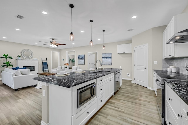 kitchen featuring stainless steel appliances, sink, a fireplace, a kitchen island with sink, and white cabinets