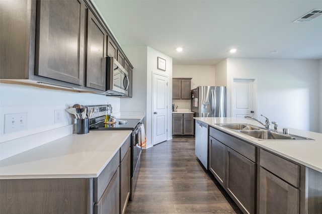 kitchen with appliances with stainless steel finishes, an island with sink, dark brown cabinets, dark hardwood / wood-style floors, and sink