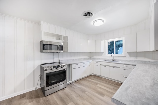 kitchen with appliances with stainless steel finishes, light wood-type flooring, sink, and white cabinetry