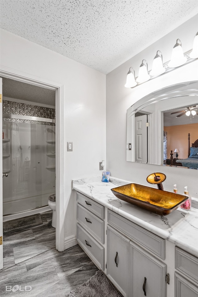 bathroom featuring vanity, walk in shower, a textured ceiling, ceiling fan, and toilet