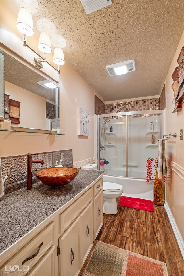 full bathroom with enclosed tub / shower combo, vanity, toilet, a textured ceiling, and hardwood / wood-style floors